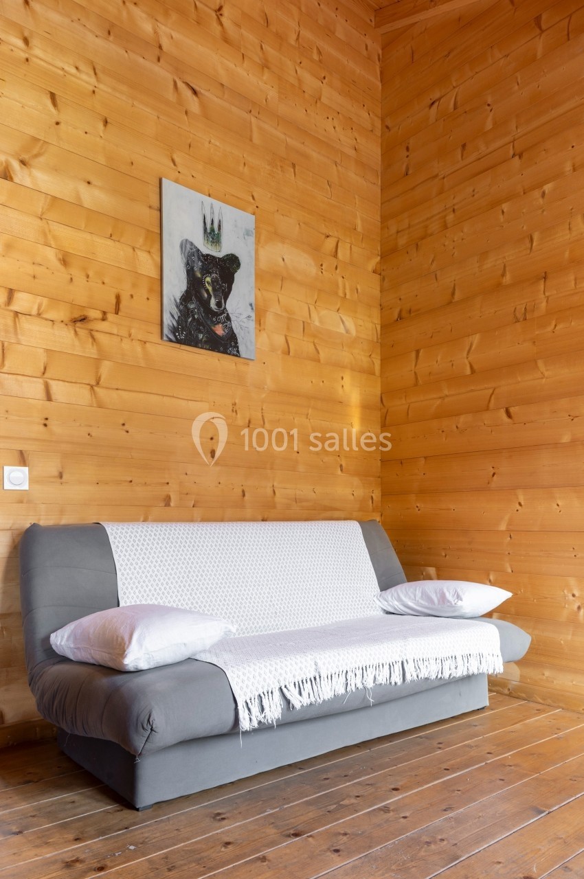 Canapé gris avec plaid blanc et coussins, placé contre un mur en bois clair, tableau décoratif au-dessus.
