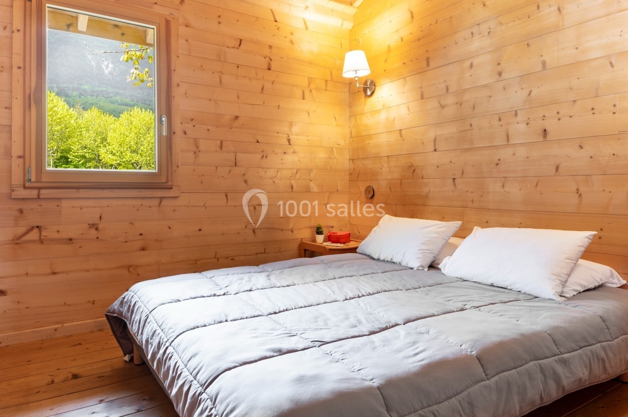 Chambre en bois avec un lit double, une lampe murale allumée et une fenêtre offrant une vue sur la montagne.