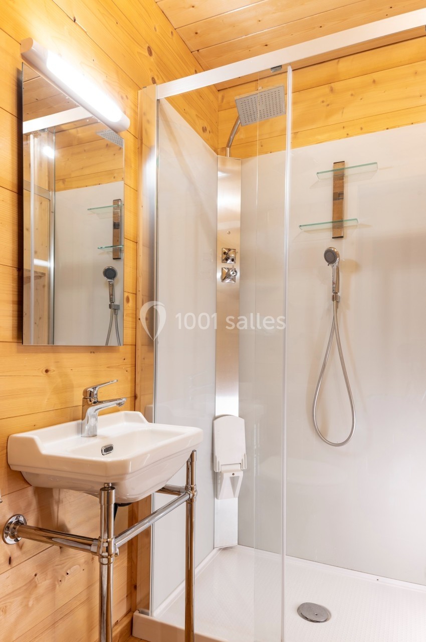 Salle de bain en bois avec une douche vitrée, un lavabo blanc et un miroir éclairé.