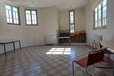 Miniature Location salle Annot (Alpes-de-Haute-Provence) - Le Pré Martin #7 Un chat assis dans un carré de lumière au sol, devant une pile de chaises empilées dans une pièce vide.