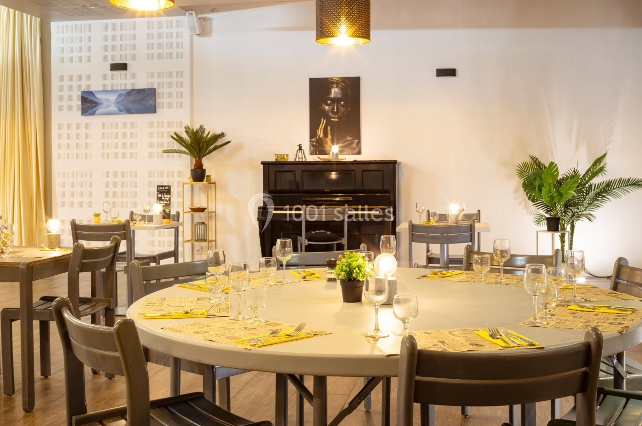 Salle de restaurant lumineuse avec tables rondes dressées, un piano noir et des plantes en décoration.