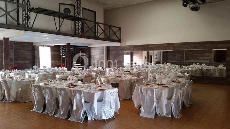 Salle de réception décorée avec des tables rondes dressées, nappes blanches et touches de rouge.