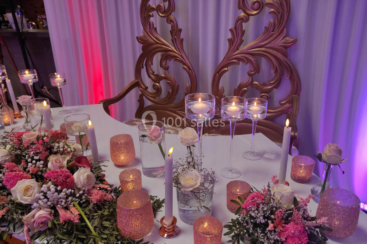 Table décorée pour un événement avec bougies, fleurs roses et blanches, et un fond orné de motifs dorés.
