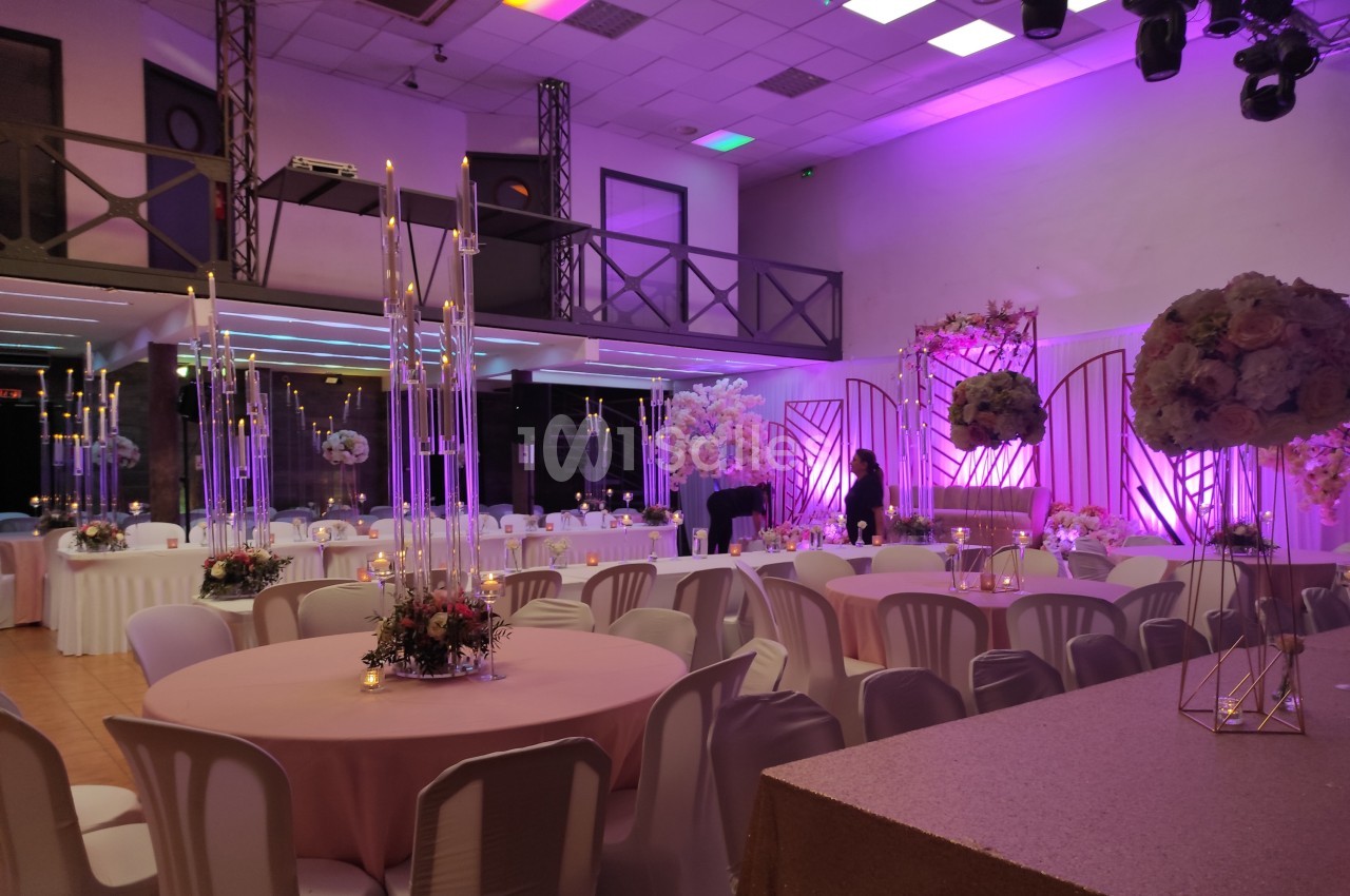 Salle de réception décorée avec des tables rondes, des chandeliers et un éclairage violet, prête pour un événement.