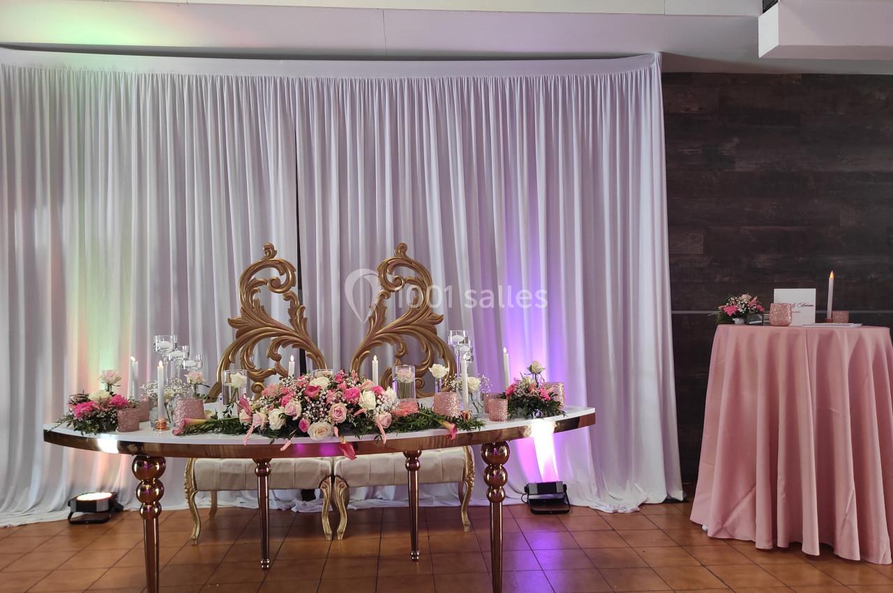 Table décorée avec des fleurs roses, bougies et ornements dorés devant un rideau blanc et un mur sombre.