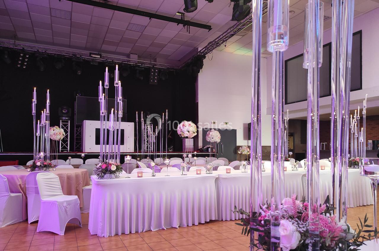 Salle de réception décorée avec des tables blanches, des chandeliers hauts et des compositions florales roses et blanches.