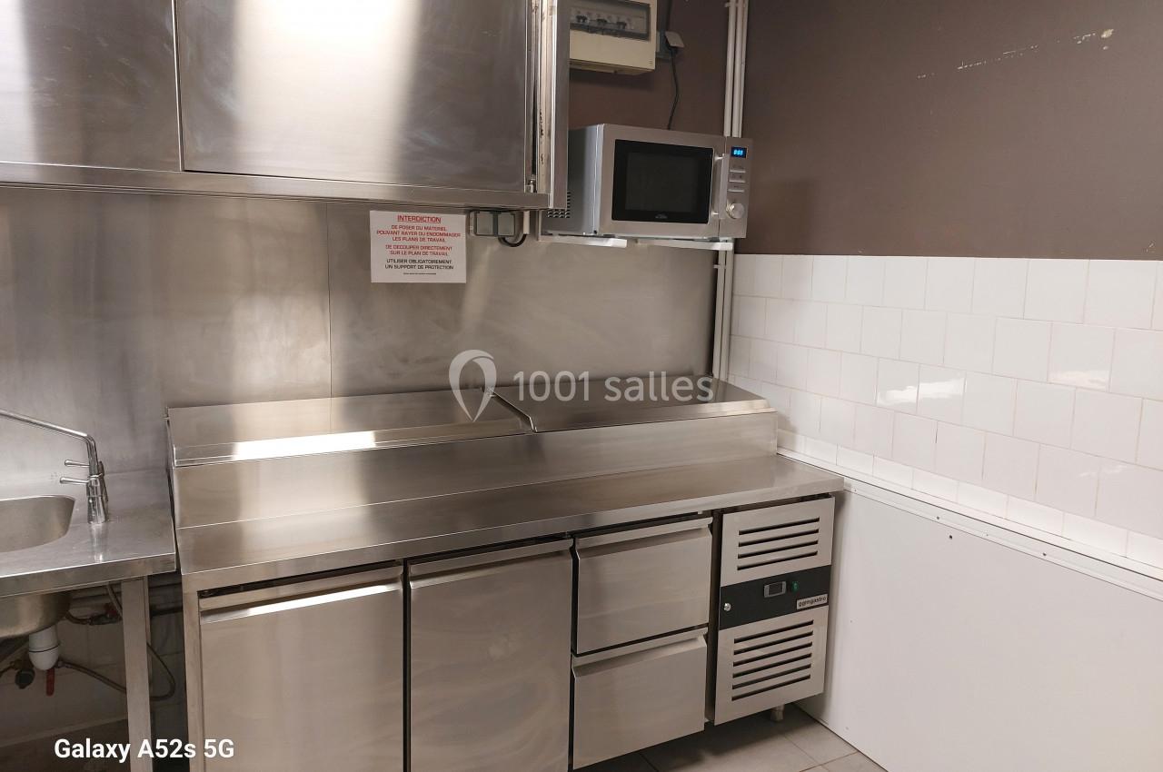 Cuisine professionnelle avec plan de travail en inox, micro-ondes mural, et meubles de rangement en acier inoxydable.