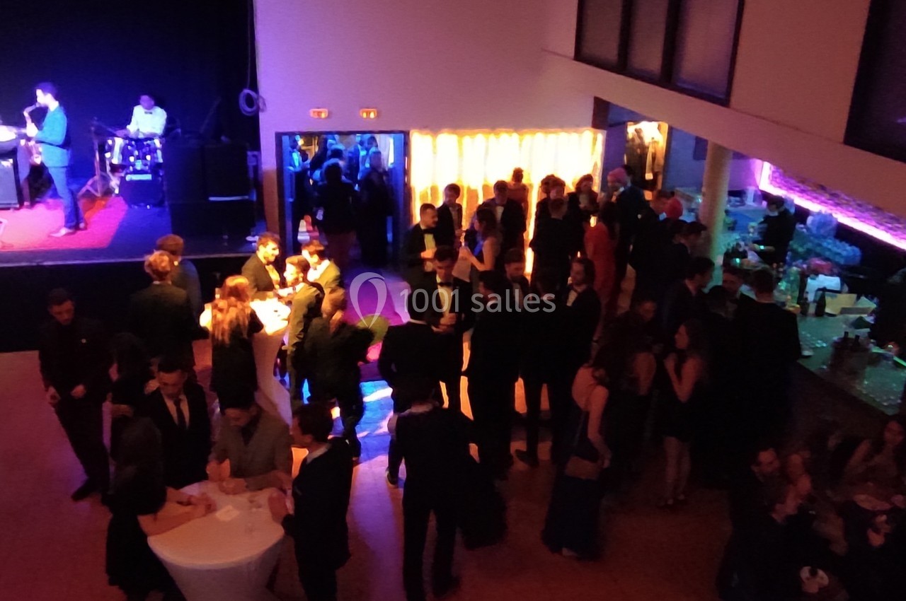 Groupe de personnes en tenue de soirée rassemblées dans une salle éclairée, avec une scène musicale en arrière-plan.