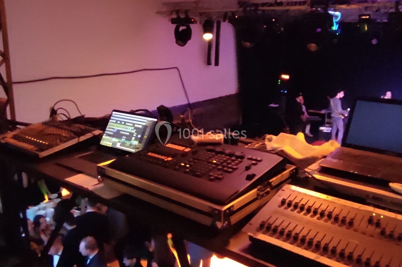 Vue d'une régie technique avec consoles de mixage et éclairage, surplombant une salle de spectacle animée.