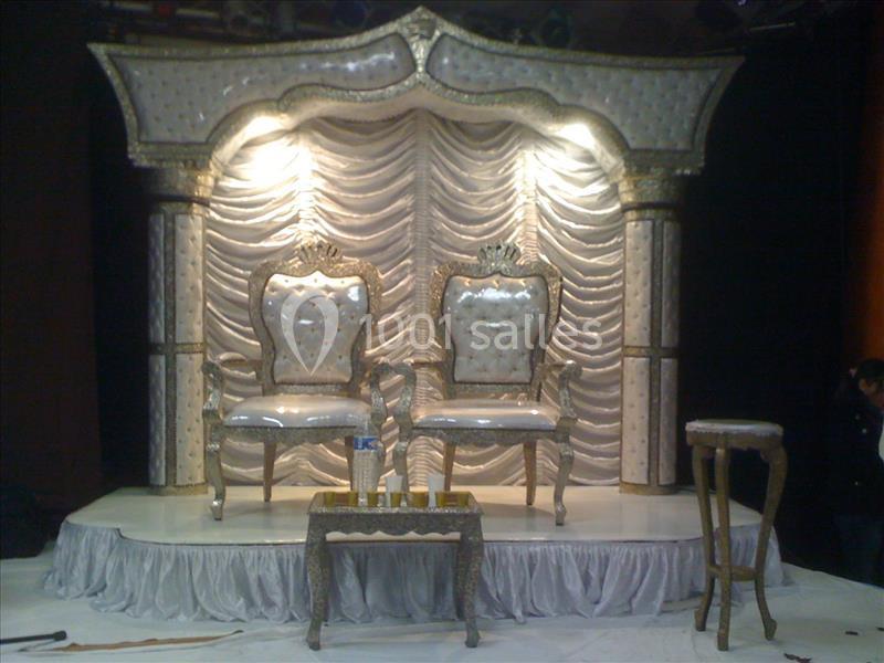 Deux fauteuils ornés et une table basse sur une scène décorée de rideaux plissés et d'un éclairage lumineux.