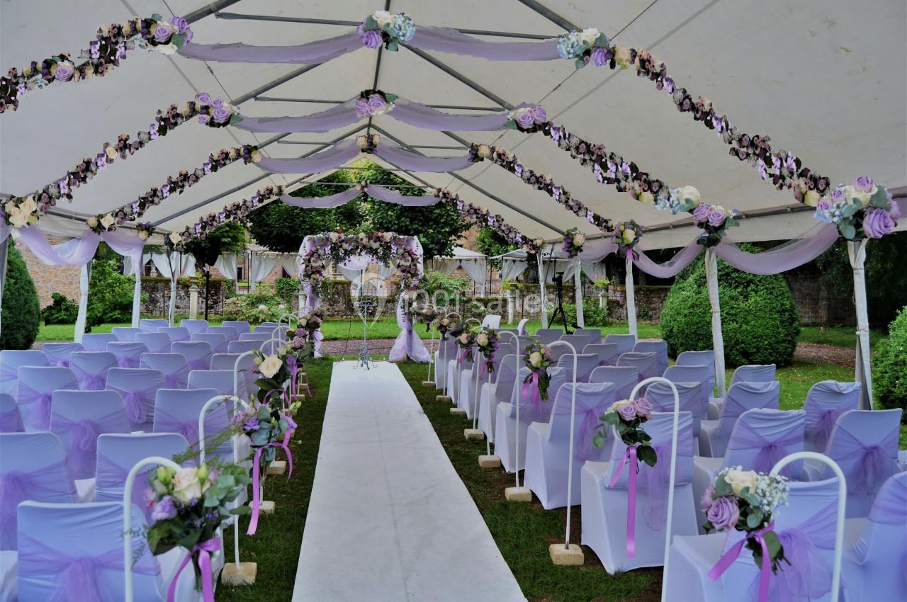 Barnum avec bancs fourni gratuitement dans le forfait pour cérémonie civile Allée centrale décorée de fleurs violettes et blanches sous une tente pour une cérémonie en plein air.