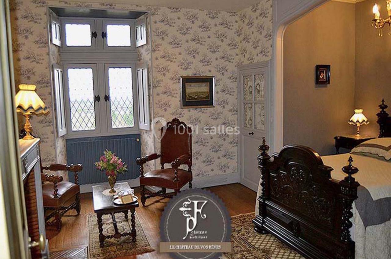 Chambre du Baron Chambre ancienne avec mobilier en bois sculpté, cheminée, deux fauteuils et fenêtre à vitraux donnant sur l'extérieur.