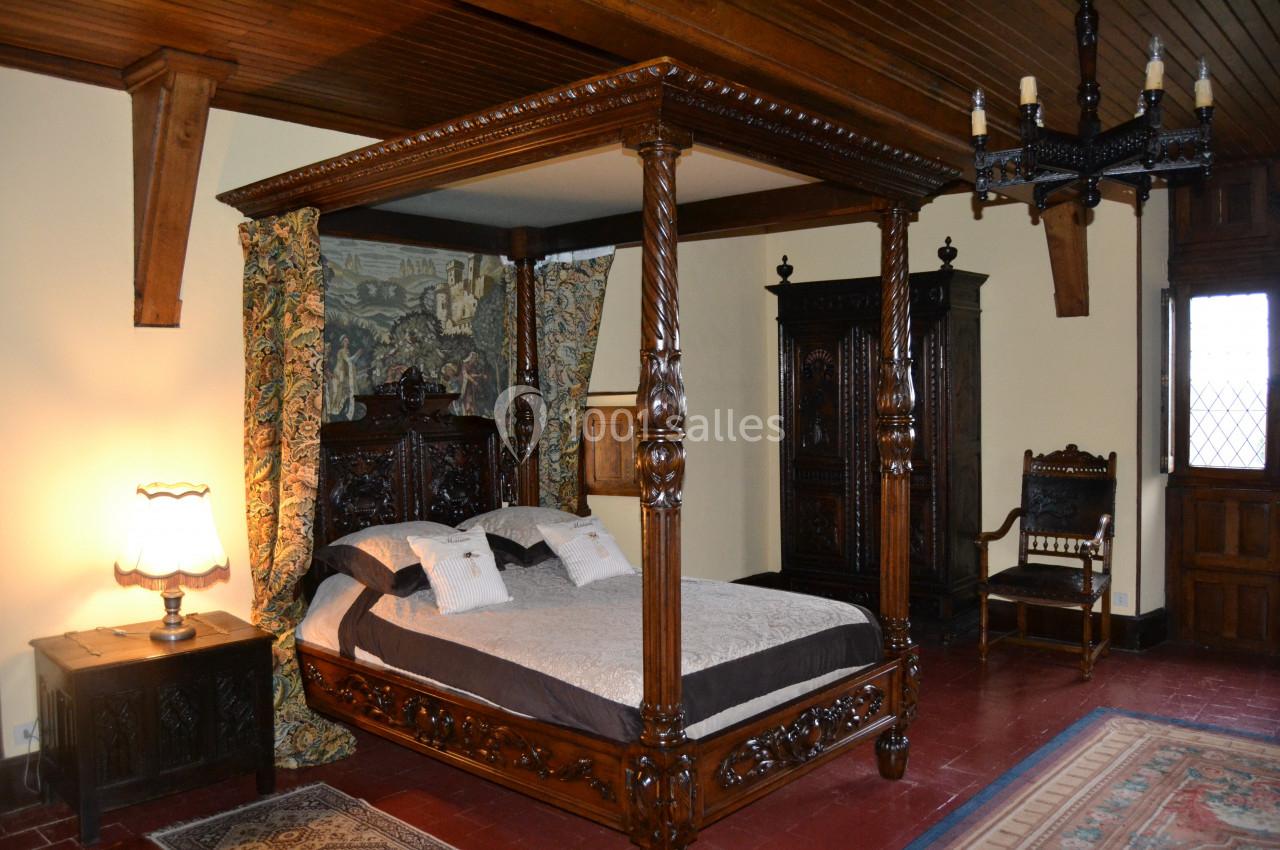Chamnbre Anne de Bretagne Lit à baldaquin en bois sculpté dans une chambre rustique avec meubles anciens et tapis au sol.