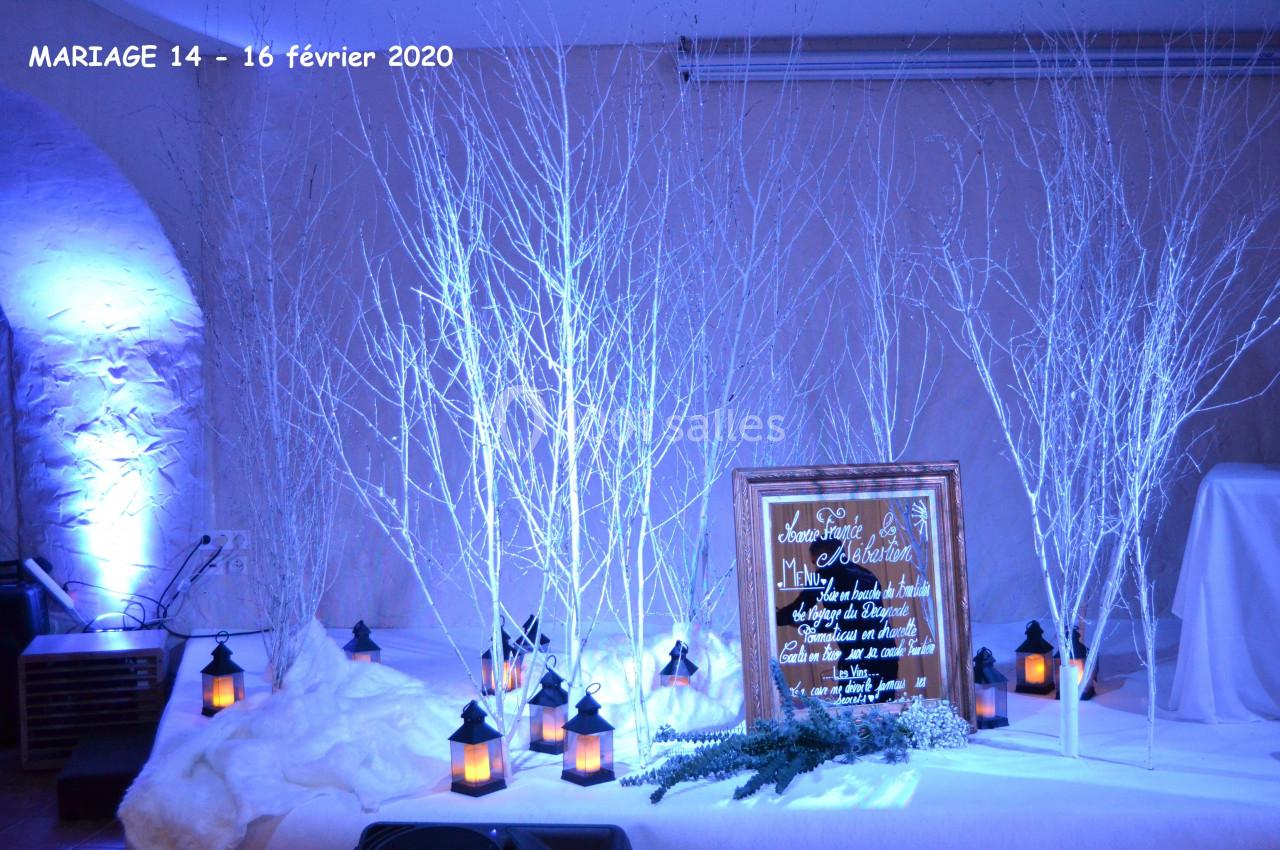 Fabuleux en hiver Décoration de mariage hivernale avec branches blanches, lanternes allumées et panneau en bois dans une ambiance bleutée.