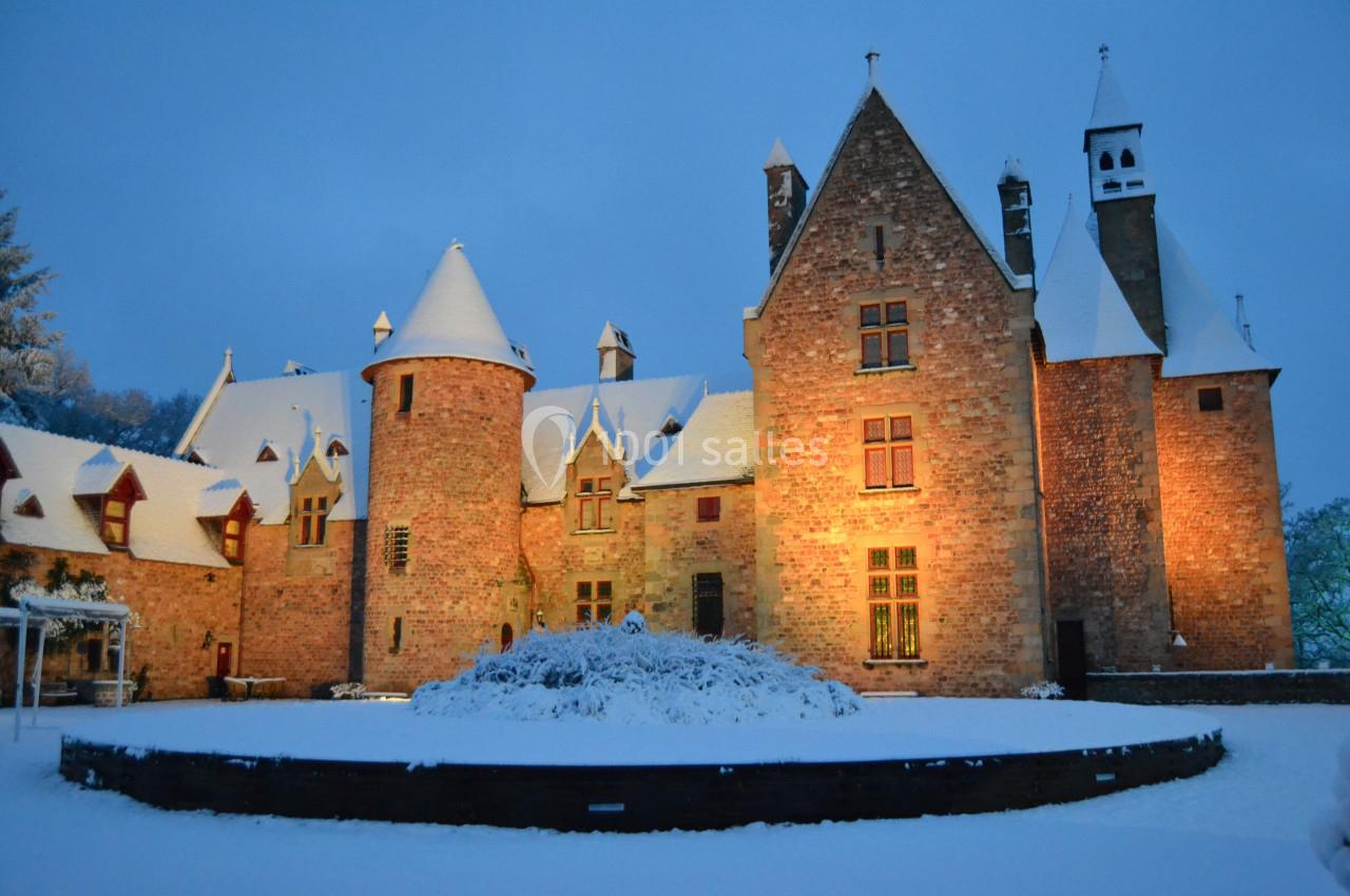 Fabuleux en hiver Château en pierre éclairé au crépuscule, entouré de neige et d'arbres sous un ciel hivernal.