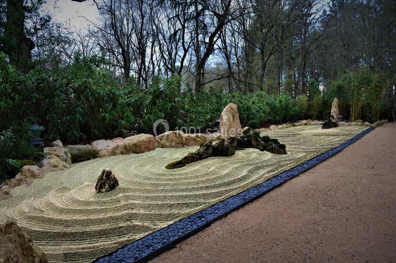 Jardin japonais Jardin zen avec gravier ratissé en motifs ondulés, pierres disposées harmonieusement et végétation en arrière-plan.