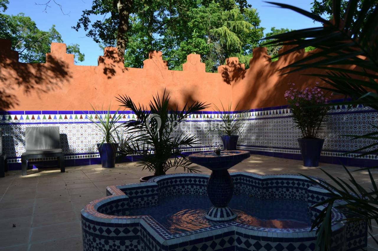 Jardin marocain Fontaine décorative au centre d'une cour ornée de carreaux colorés, entourée de plantes et d'un mur ocre.