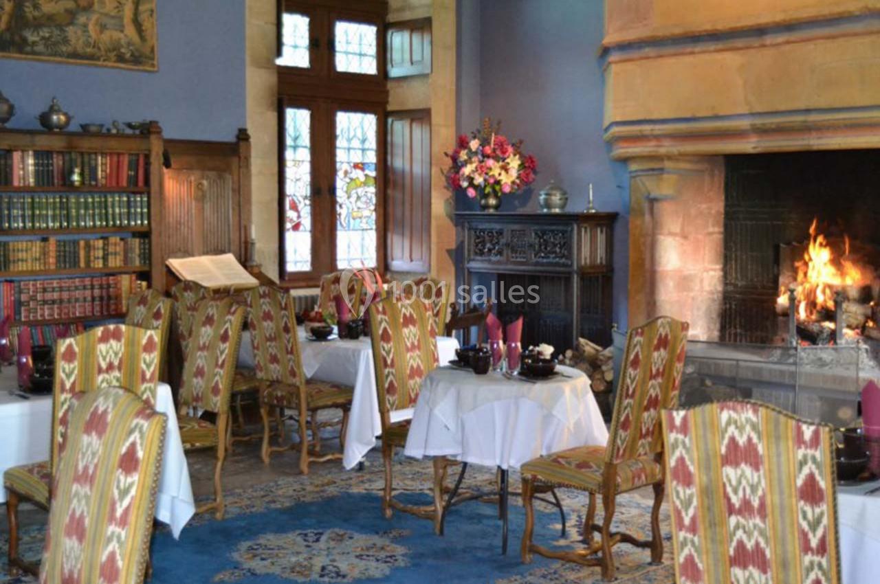 Petites réceptions 30 personnes maxi Salle à manger chaleureuse avec cheminée allumée, tables dressées, chaises à motifs et bibliothèque en arrière-plan.