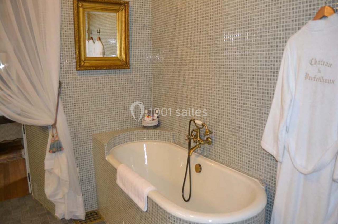 Salle de bain chambre Pompadour Salle de bain avec baignoire blanche, robinetterie dorée, miroir encadré et murs en mosaïque grise.