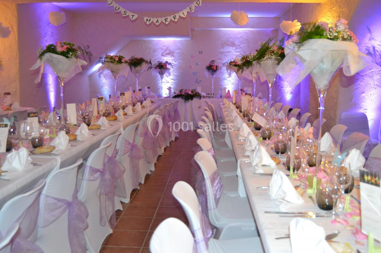 Salle de mariage 110 personnes autour de tables Salle de réception décorée pour un mariage, avec longues tables dressées, nappes blanches et fleurs violettes.