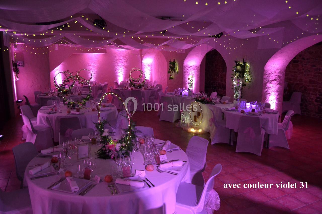 Salle de mariage 110 personnes autour de tables Salle de réception décorée avec des guirlandes lumineuses, des nappes blanches et une ambiance lumineuse violette.