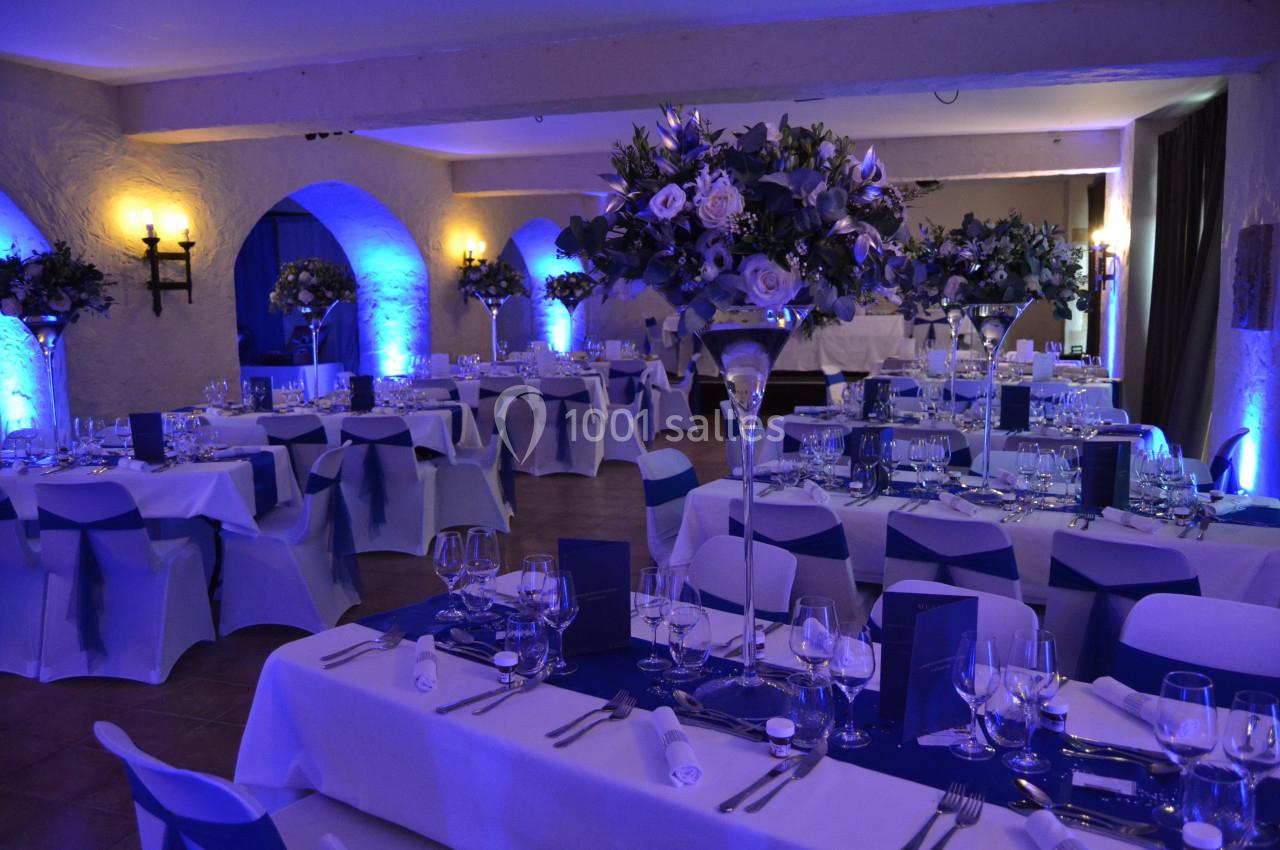 Salle de mariage 110 personnes autour de tables Salle de réception élégamment décorée avec des tables dressées, des fleurs et un éclairage bleu tamisé.
