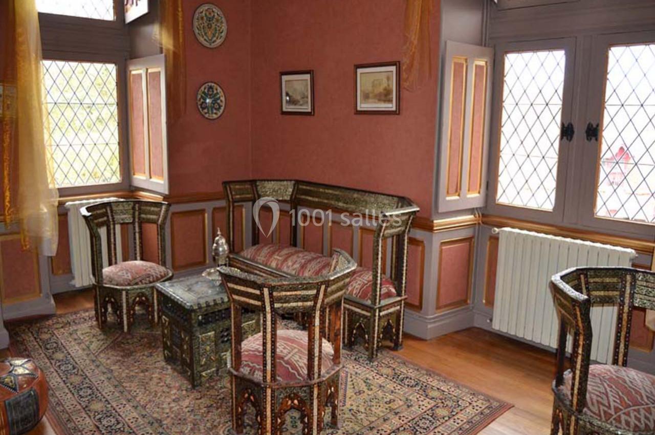 salon chambre Shéhérazade Salon décoré dans un style oriental avec mobilier en bois incrusté, tapis coloré et fenêtres à vitraux.