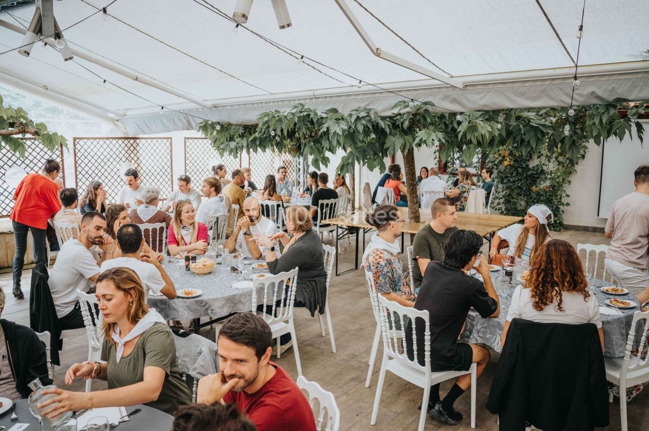 Des personnes assises à des tables dans une grande salle lumineuse, partageant un repas dans une ambiance conviviale.