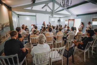 Deux lits simples avec draps blancs, séparés par une table de chevet en bois, éclairés par deux appliques murales.
