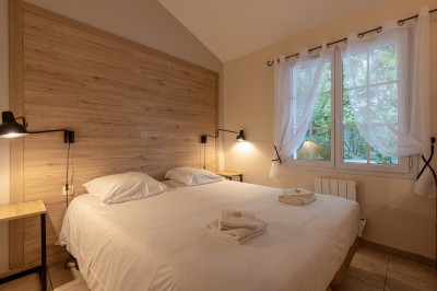 Deux lits simples avec draps blancs, séparés par une table de chevet en bois, éclairés par deux appliques murales.