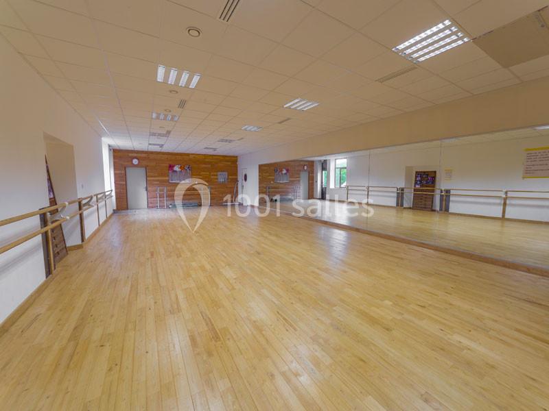 Salle de danse lumineuse avec parquet en bois, miroirs sur un mur et barres fixées aux parois latérales.