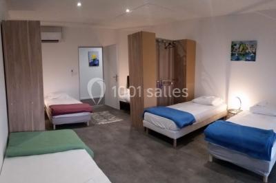 Lit double avec draps blancs, coussins décoratifs noirs et blancs, lampe de chevet allumée et tableau mural coloré.