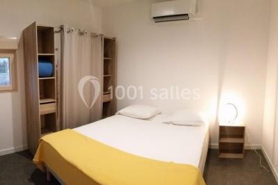 Lit double avec draps blancs, coussins décoratifs noirs et blancs, lampe de chevet allumée et tableau mural coloré.