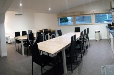 Lit double avec draps blancs, coussins décoratifs noirs et blancs, lampe de chevet allumée et tableau mural coloré.