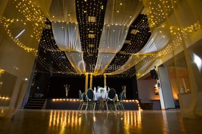 Lit double avec draps blancs, coussins décoratifs noirs et blancs, lampe de chevet allumée et tableau mural coloré.