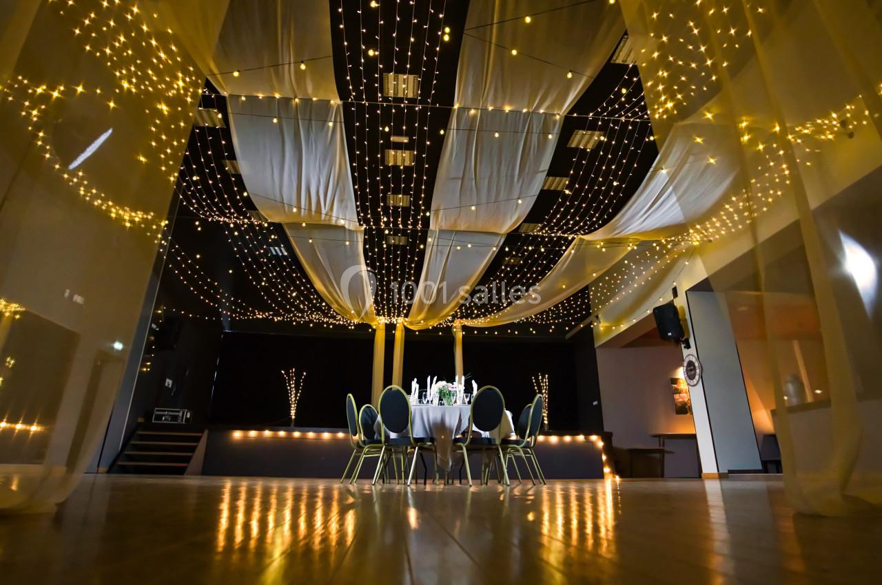 Salle décorée avec des guirlandes lumineuses suspendues et des voilages, entourant une table ronde dressée.