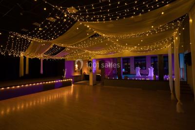 Lit double avec draps blancs, coussins décoratifs noirs et blancs, lampe de chevet allumée et tableau mural coloré.