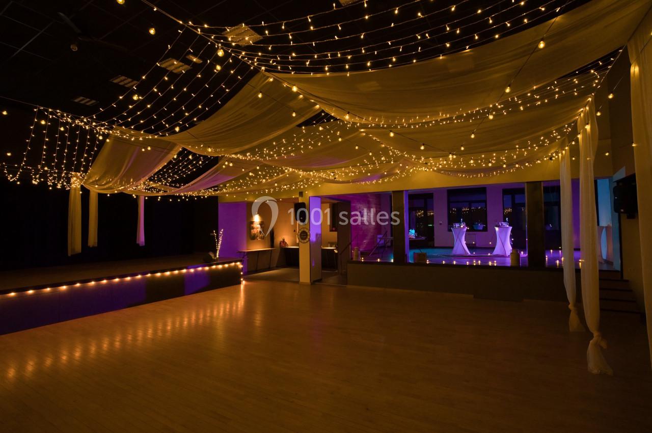 Salle de réception décorée avec des guirlandes lumineuses suspendues et des drapés, éclairage tamisé.