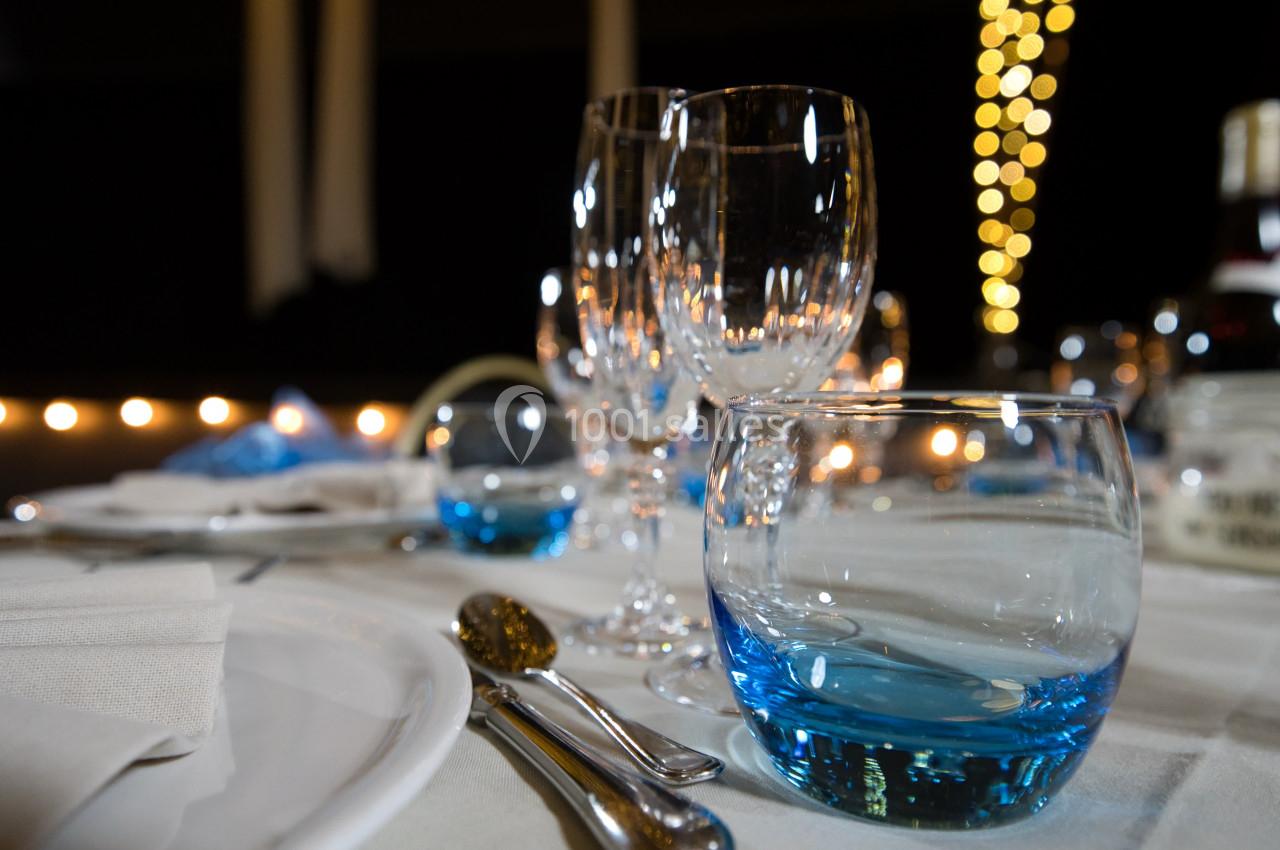 Table dressée avec des verres, couverts et assiettes, éclairée par des lumières tamisées en arrière-plan.