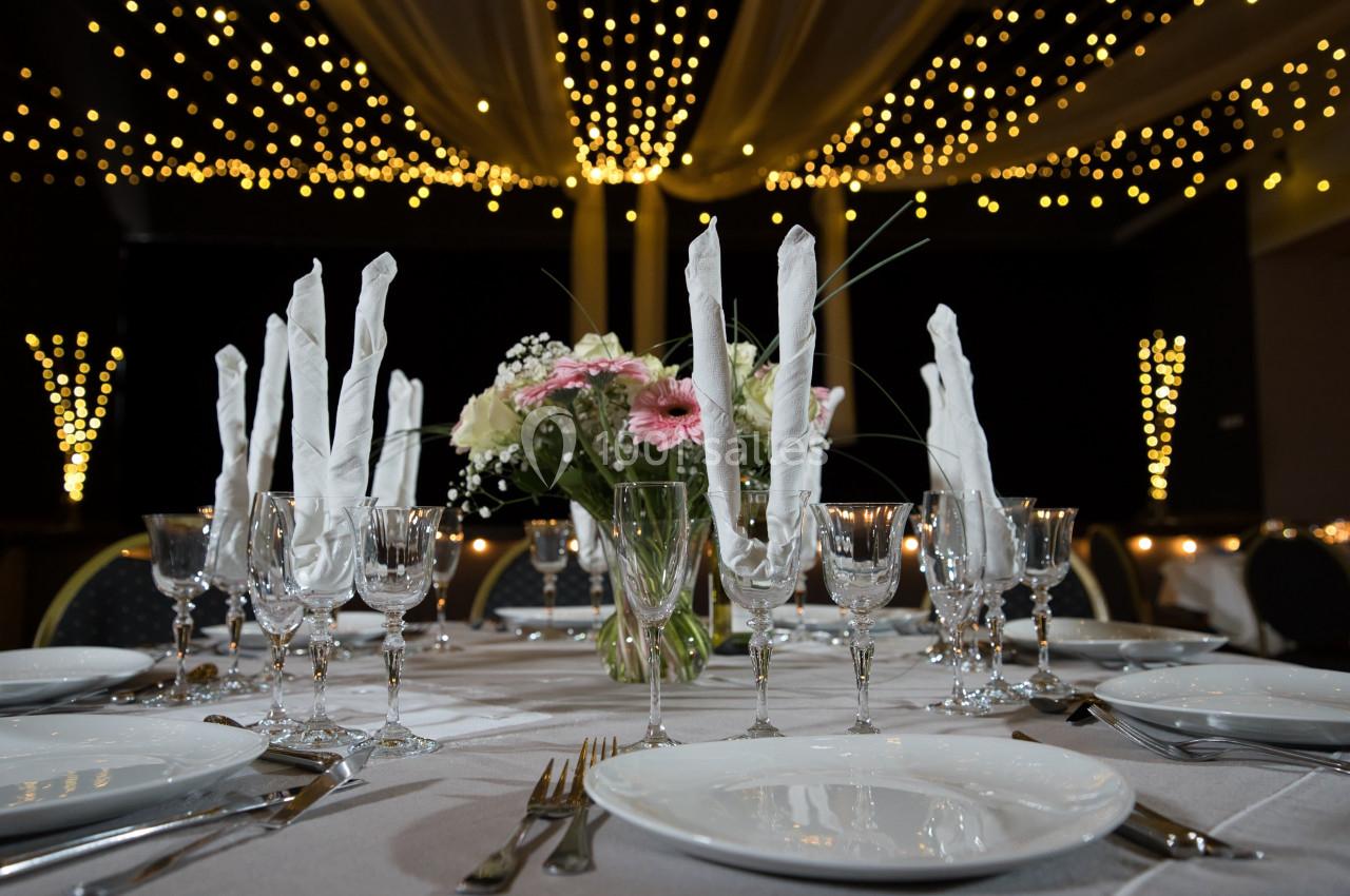 Table élégamment dressée avec vaisselle blanche, verres en cristal, serviettes pliées et bouquet de fleurs, sous des…