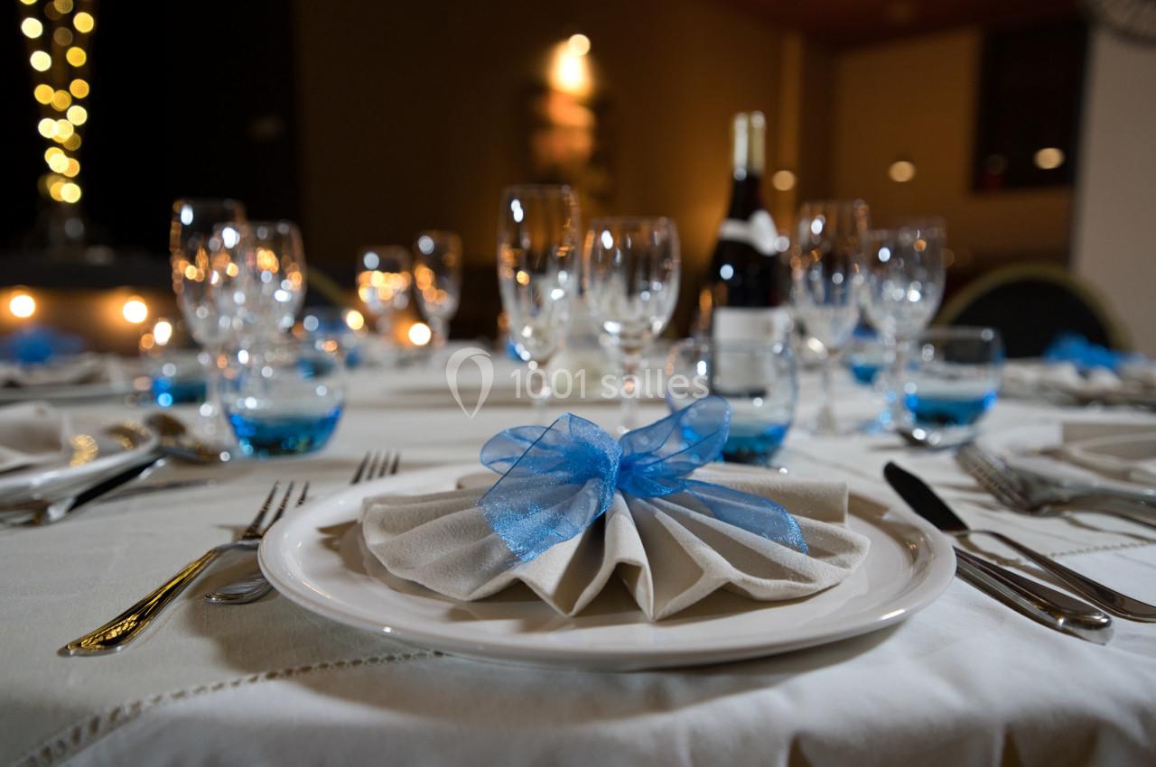 Table dressée avec élégance, serviette pliée ornée d'un ruban bleu, verres et couverts disposés soigneusement.