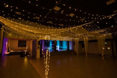 Lit double avec draps blancs, coussins décoratifs noirs et blancs, lampe de chevet allumée et tableau mural coloré.