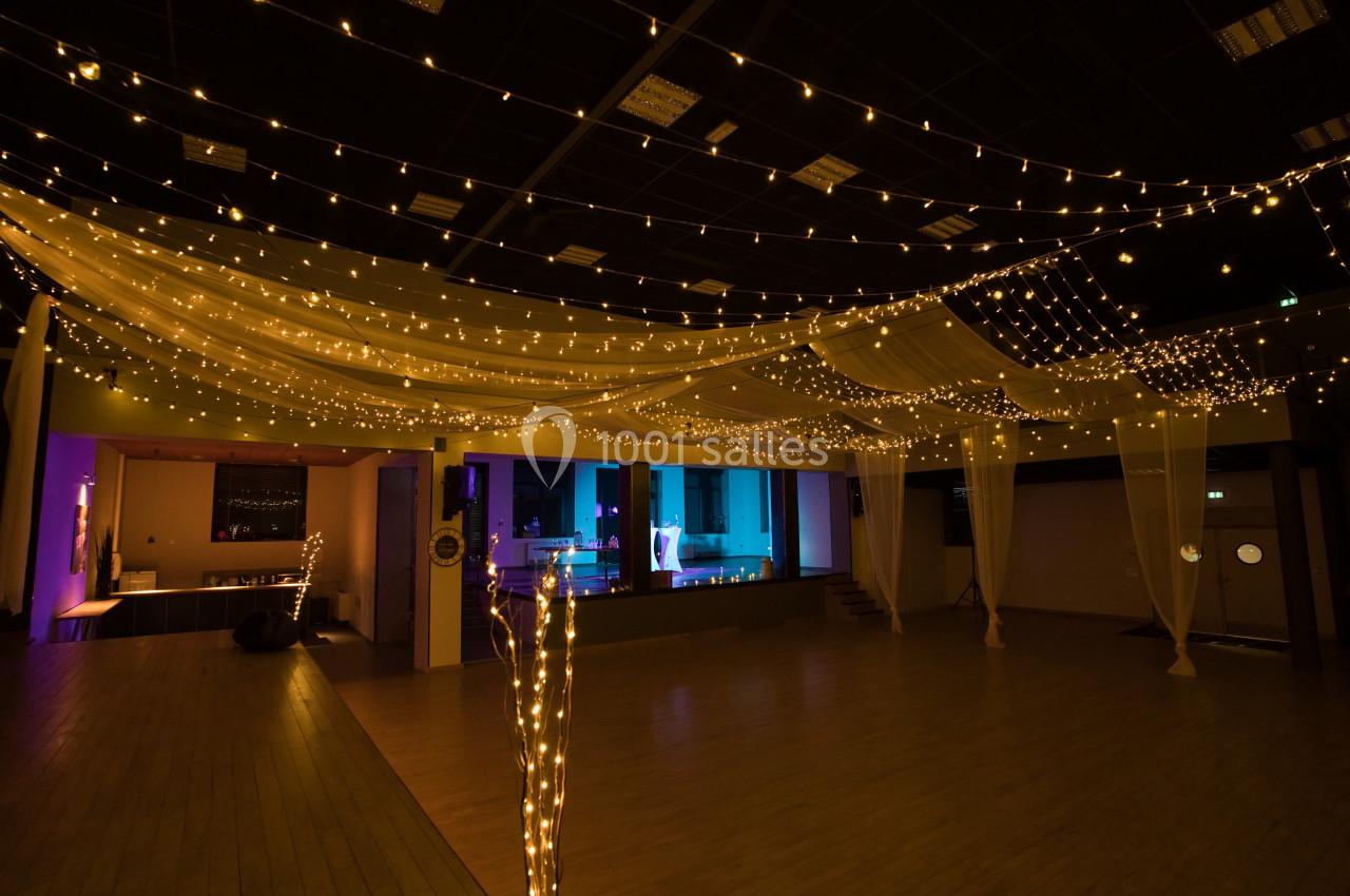 Salle de réception décorée avec des guirlandes lumineuses suspendues et un éclairage tamisé.