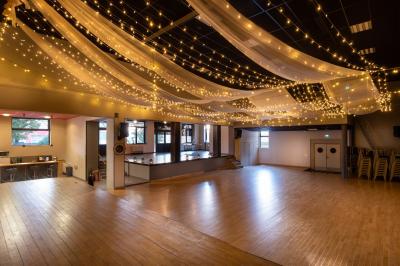 Lit double avec draps blancs, coussins décoratifs noirs et blancs, lampe de chevet allumée et tableau mural coloré.