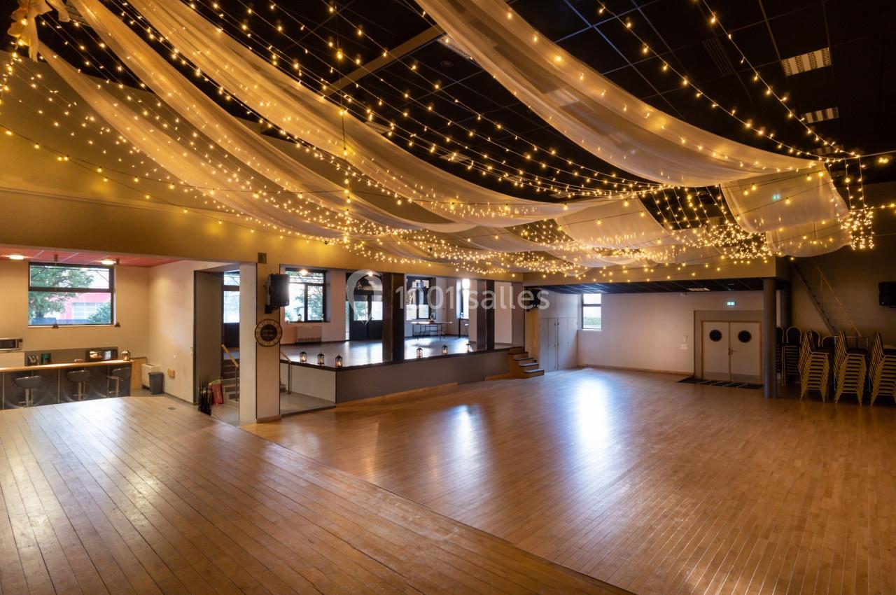 Salle spacieuse avec parquet, rideaux lumineux suspendus et espace aménagé pour des événements ou activités.