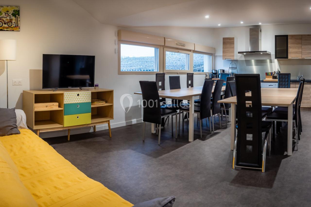 Vue d'une pièce lumineuse avec salon, canapé jaune, télévision, et cuisine ouverte équipée avec table à manger.