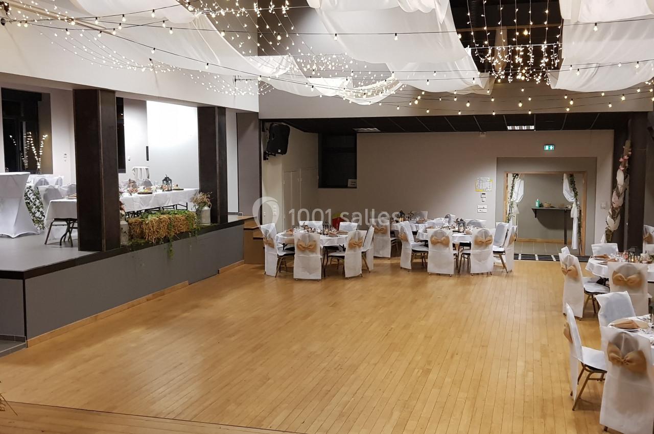 Salle de réception décorée avec des guirlandes lumineuses, des tables dressées et une scène en arrière-plan.