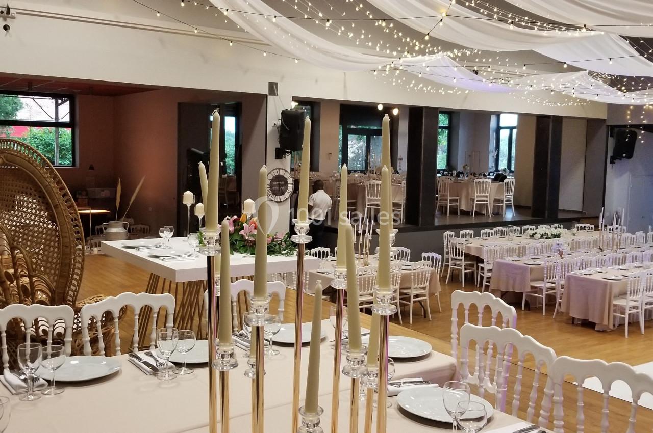 Salle de réception décorée avec des tables dressées, des chaises blanches et un plafond orné de guirlandes lumineuses.