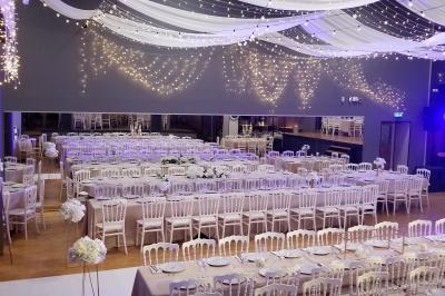 Lit double avec draps blancs, coussins décoratifs noirs et blancs, lampe de chevet allumée et tableau mural coloré.