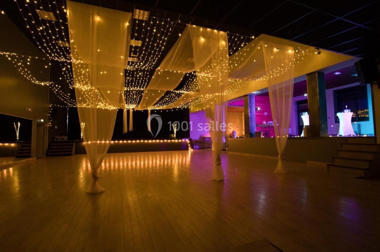 Salle de réception avec parquet, éclairage tamisé et guirlandes lumineuses suspendues au plafond.